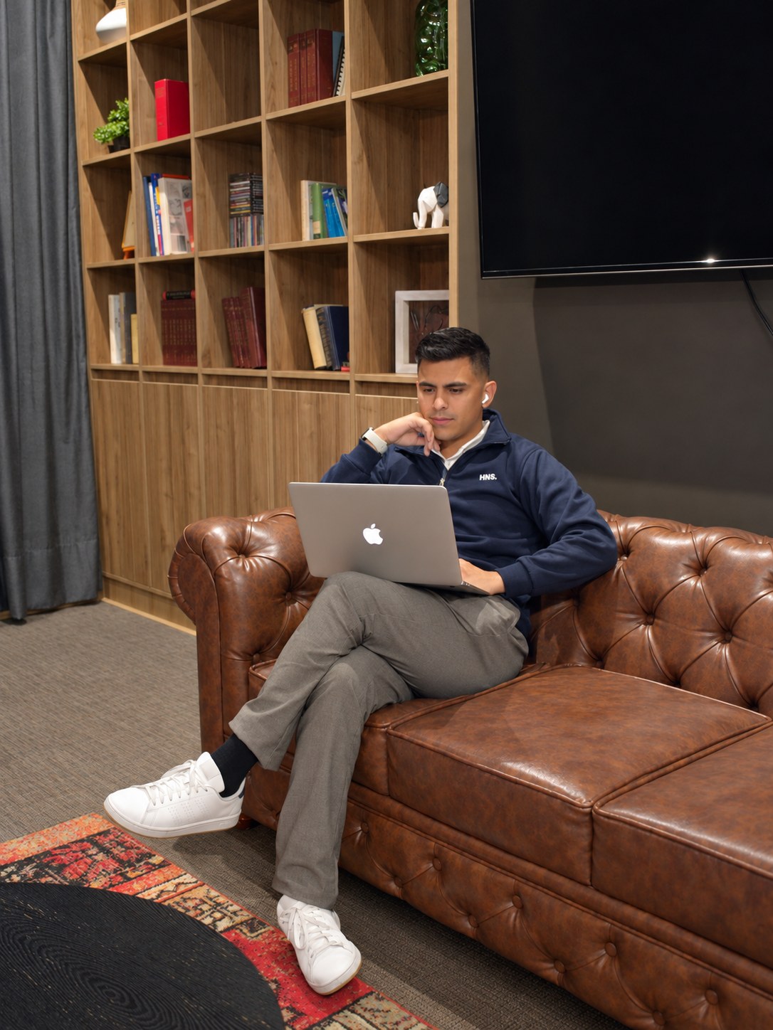 Johan Angel trabajando en su portátil en un sofá de cuero, en una oficina con estanterías